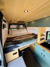 RV rental's modern interior: bamboo ceiling, cozy bed with patterned blanket, kitchenette & smart storage.