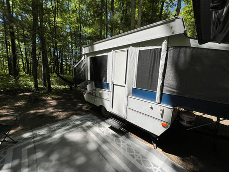 Pop-up camper RV rental ready for adventure at a sunny, wooded campsite. Perfect for outdoor getaways.