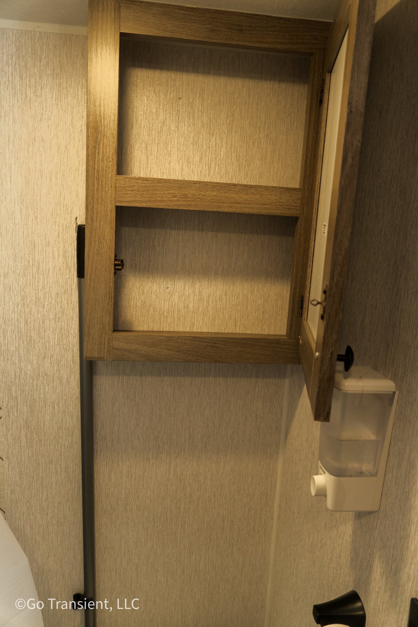 RV rental bathroom: Open wood cabinet with shelf and wall-mounted soap dispenser. Great for storage.