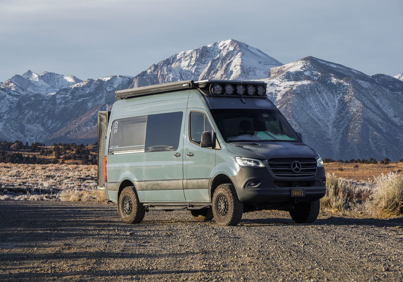 Custom 4x4 Mercedes Sprinter camper van RV rental, parked on a dirt road with majestic snowy mountains.