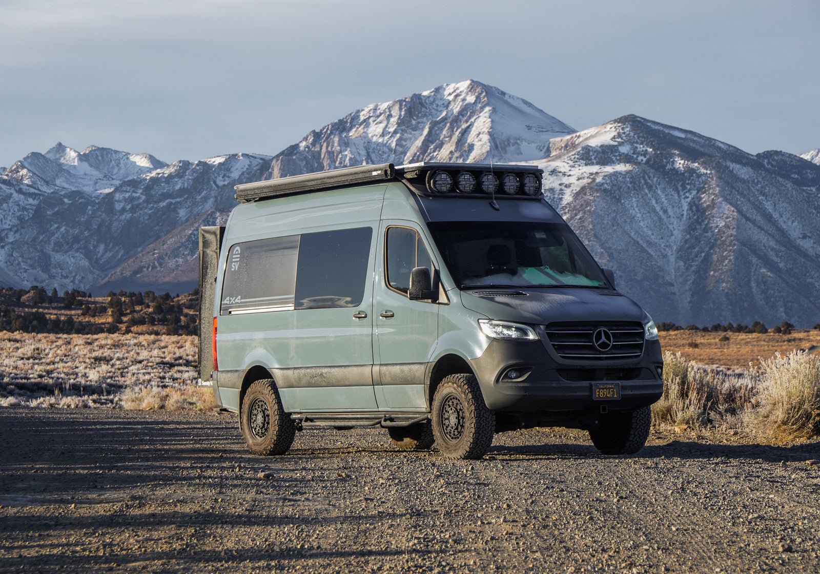 Custom 4x4 Mercedes Sprinter camper van RV rental, parked on a dirt road with majestic snowy mountains.