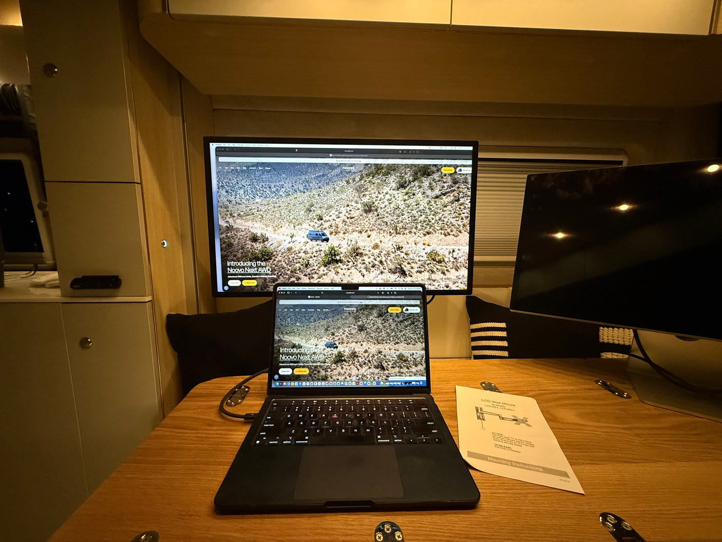 Inside an RV rental, a laptop & monitor show the "Noovo Next AWD" camper van, creating a mobile office setup.