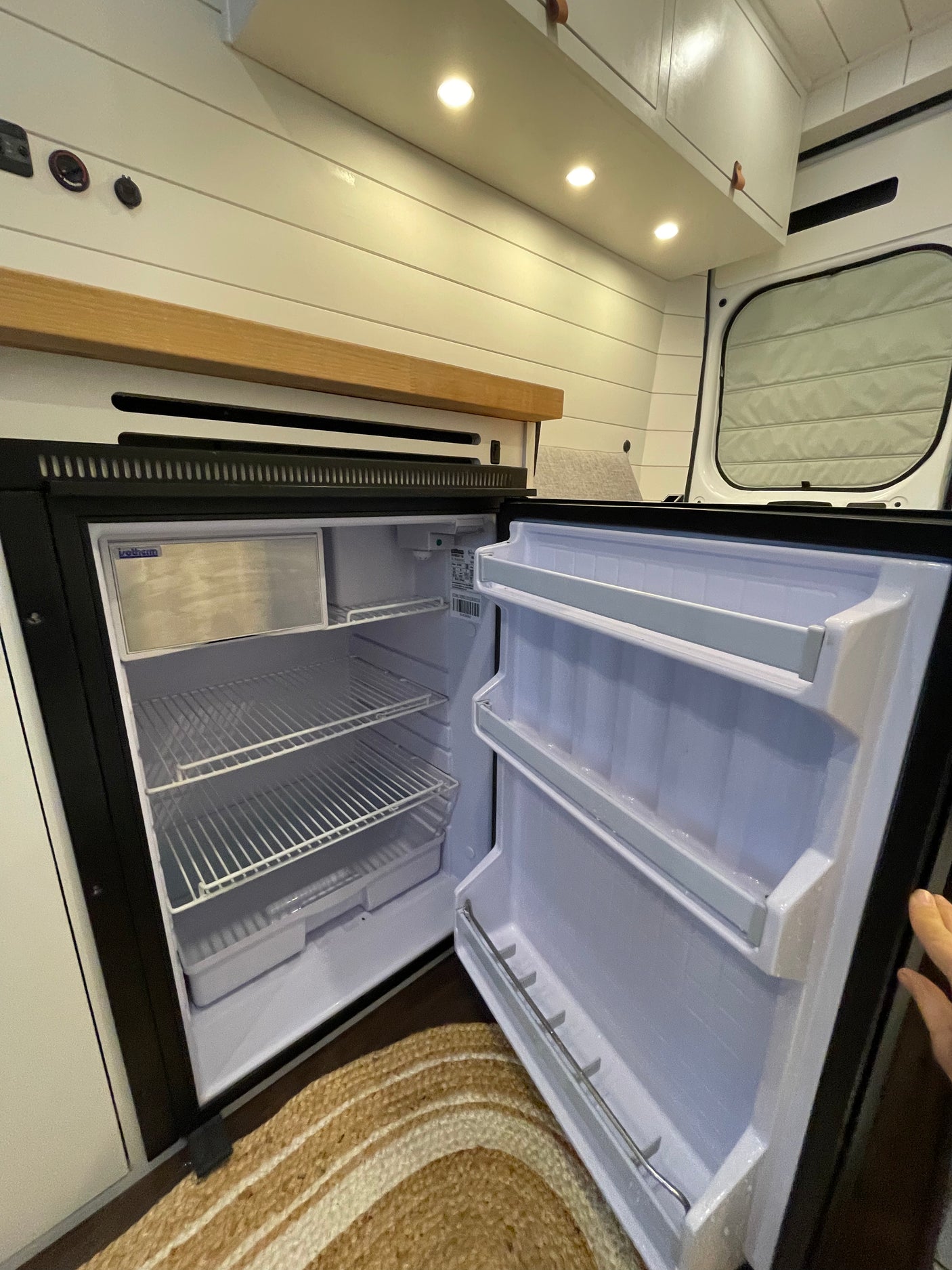 An open refrigerator in a well-lit RV rental, revealing neat interior shelves and a small freezer for convenience.