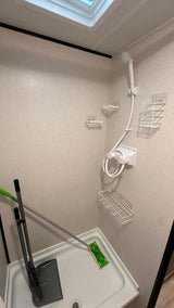 Inside an RV rental, this compact shower features a handheld shower head, wire caddies, and convenient storage for a broom and mop.