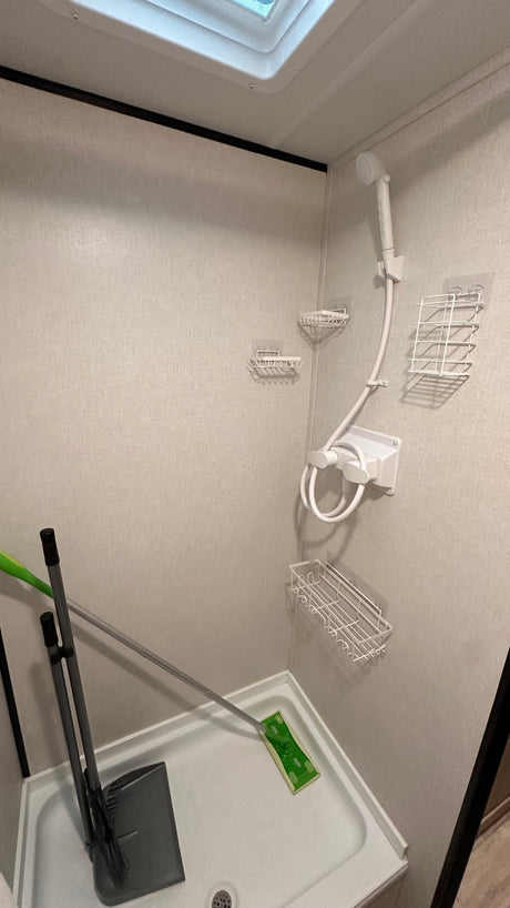 Inside an RV rental, this compact shower features a handheld shower head, wire caddies, and convenient storage for a broom and mop.