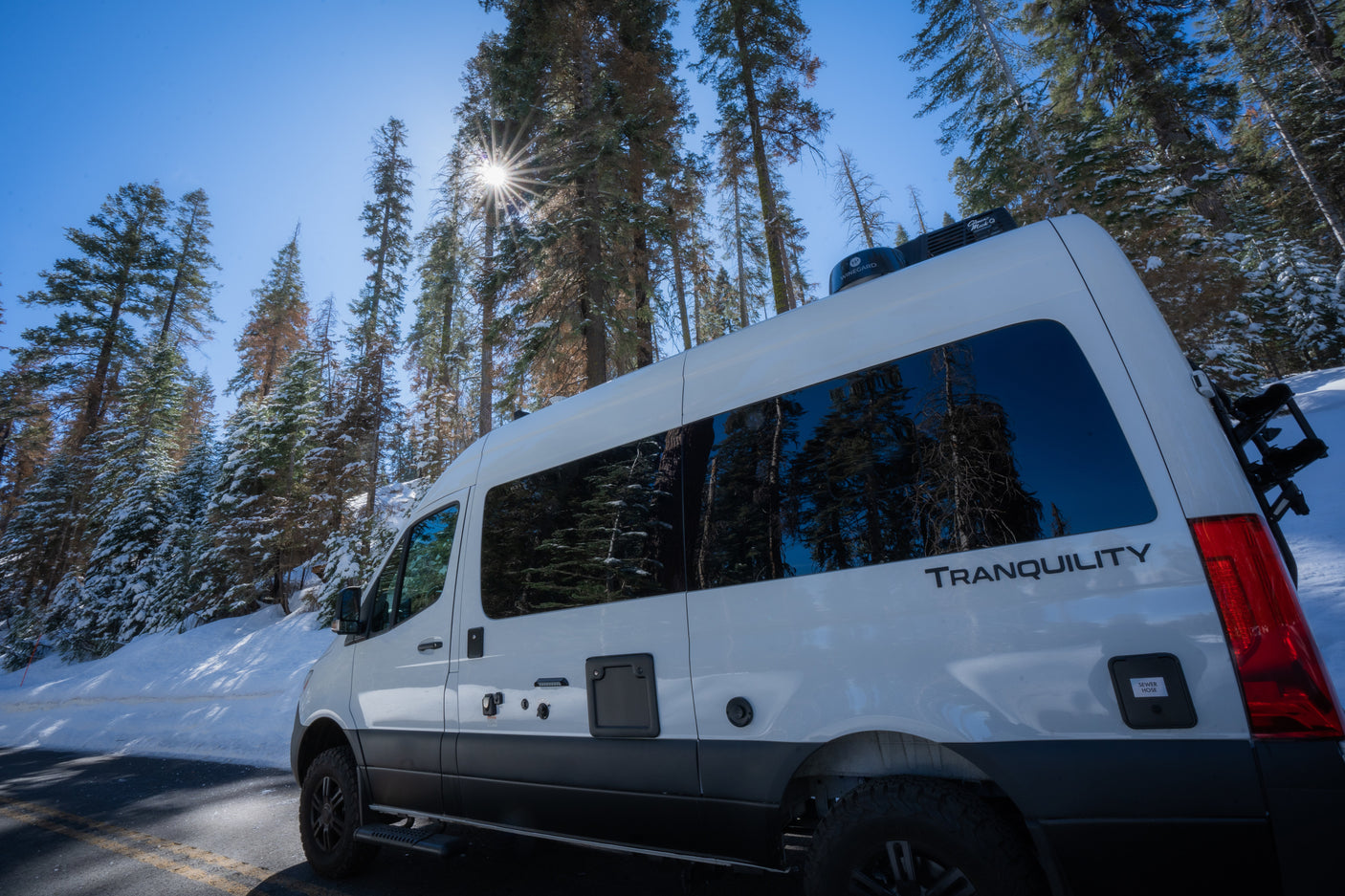 This white RV rental is parked by snow-covered trees on a sunny winter day, ready for adventure on the open road.