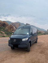 Dark Mercedes Sprinter RV rental van parked on dirt, with rugged mountains in the background.