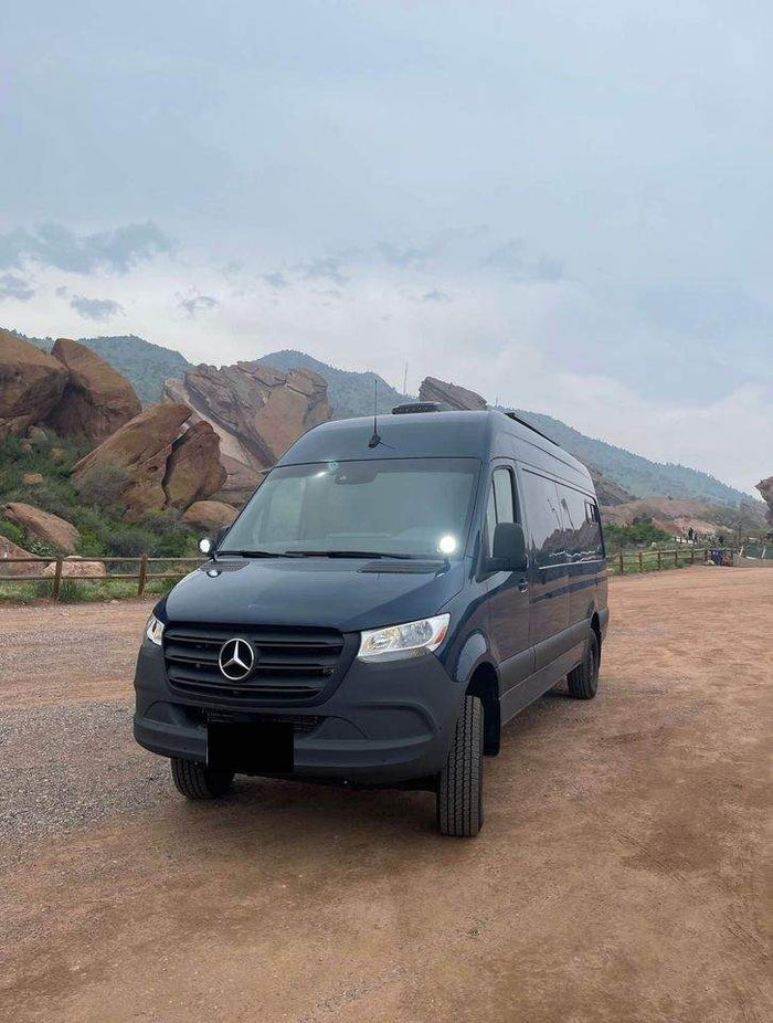 Dark Mercedes Sprinter RV rental van parked on dirt, with rugged mountains in the background.