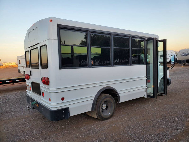 White shuttle bus, ideal for an RV rental or camper conversion, with doors open on a gravel lot. Other RVs nearby. — photo 7