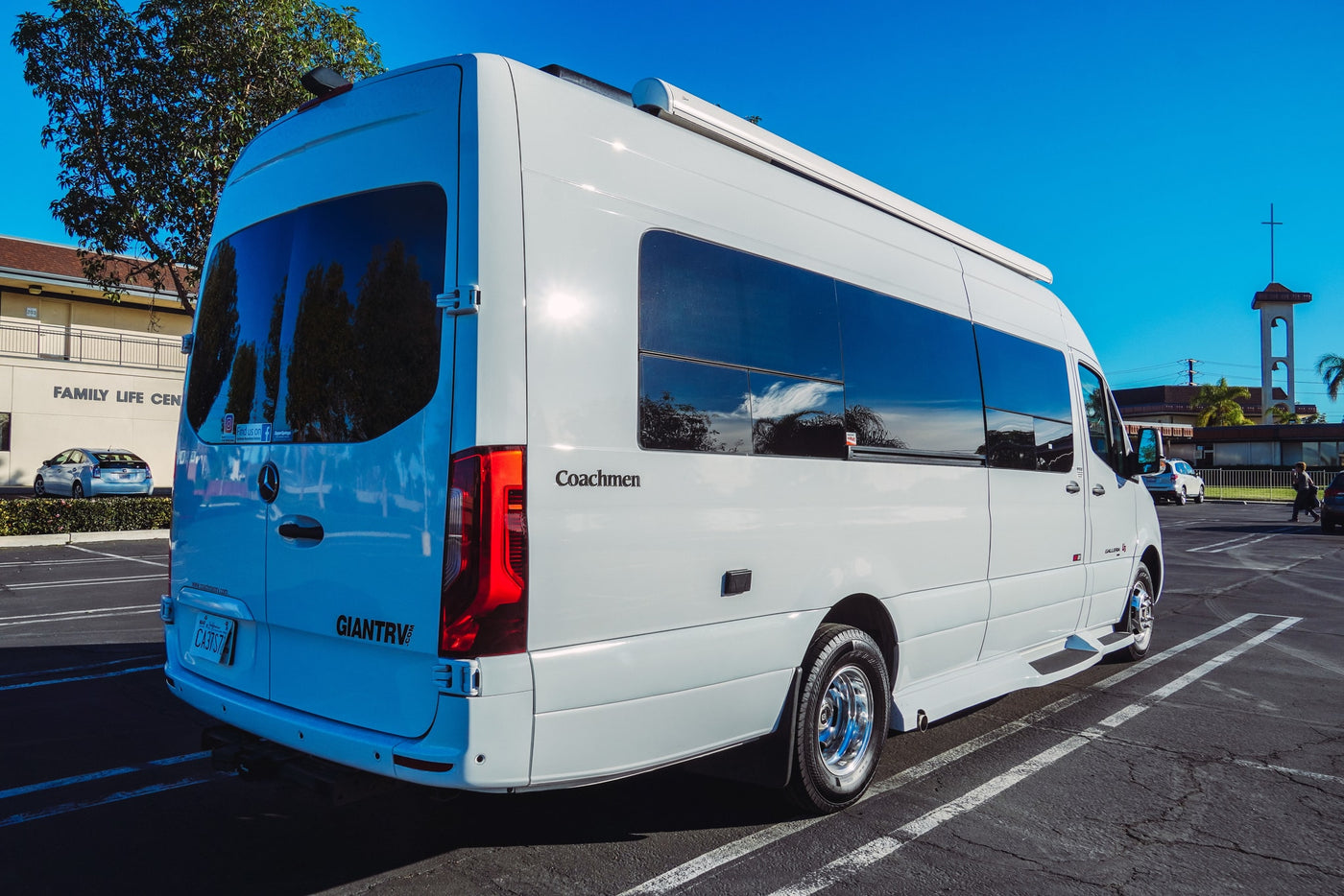 Bright white Coachmen camper van, an rv rental, parked in a sunny lot. Blue sky and trees reflect on its windows. — photo 12