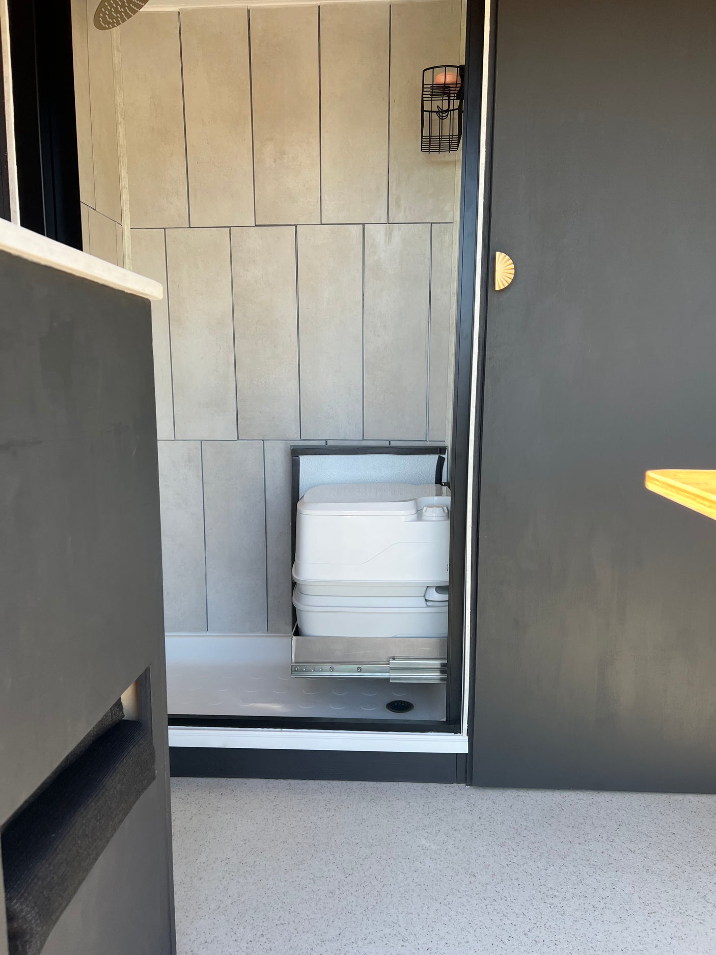 RV rental bathroom with modern grey tiles, shower, and space-saving pull-out portable toilet on sliders.