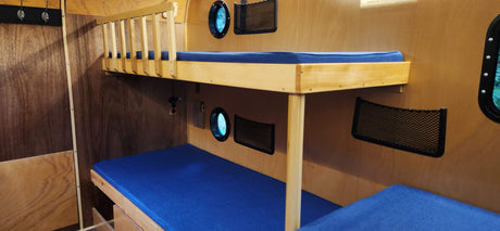Inside an RV rental: compact wooden bunk beds with blue mattresses, porthole windows, and mesh storage. Perfect for adventurers.