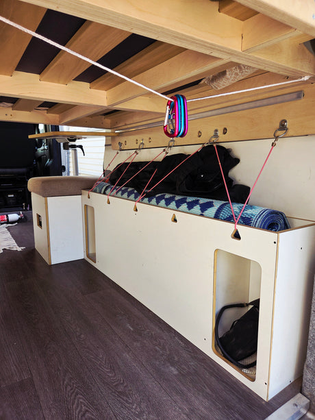 RV rental: Van interior, custom bed above storage bench with items secured by bungees & carabiners.