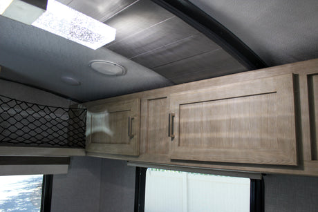 RV rental interior featuring light wood overhead cabinets, net storage, ceiling lights, speakers, and window blinds.