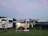 RV rental site at dusk: a Sunseeker motorhome, silver Airstream trailer, and Jeep parked on a grassy field.