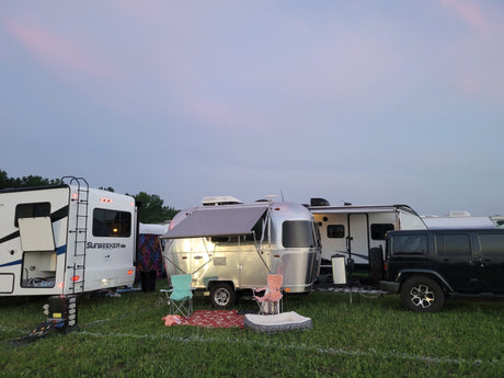 RV rental site at dusk: a Sunseeker motorhome, silver Airstream trailer, and Jeep parked on a grassy field.