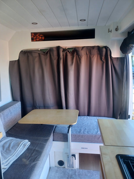 RV rental interior: a versatile dining area with bench seating, an adjustable table, privacy curtains, and overhead storage.