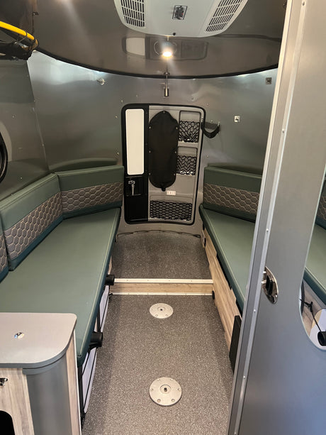 RV rental: Green cushioned benches with honeycomb pattern, textured grey floor, and a rear door with storage nets. Perfect for travel.