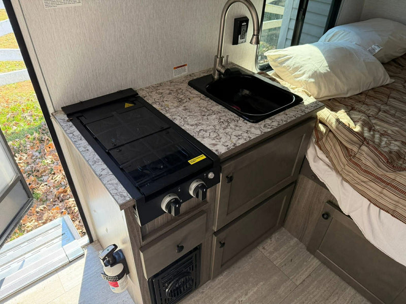 Cozy RV rental interior: compact kitchen with a two-burner stove, sink, and an inviting bed space. — photo 7