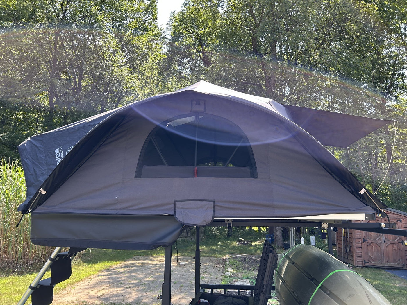 Three-quarter view of the same rooftop tent set up in evening light with the awning canopy propped out over the side door, showing the tent profile, the guy line and the mounting rails on the rack below — photo 2