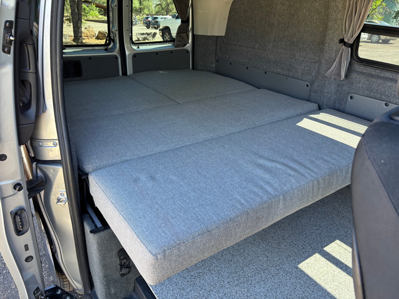 RV rental: Interior of a camper van with a gray modular bed and carpeted walls. Power outlets visible for comfy travel. — photo 6
