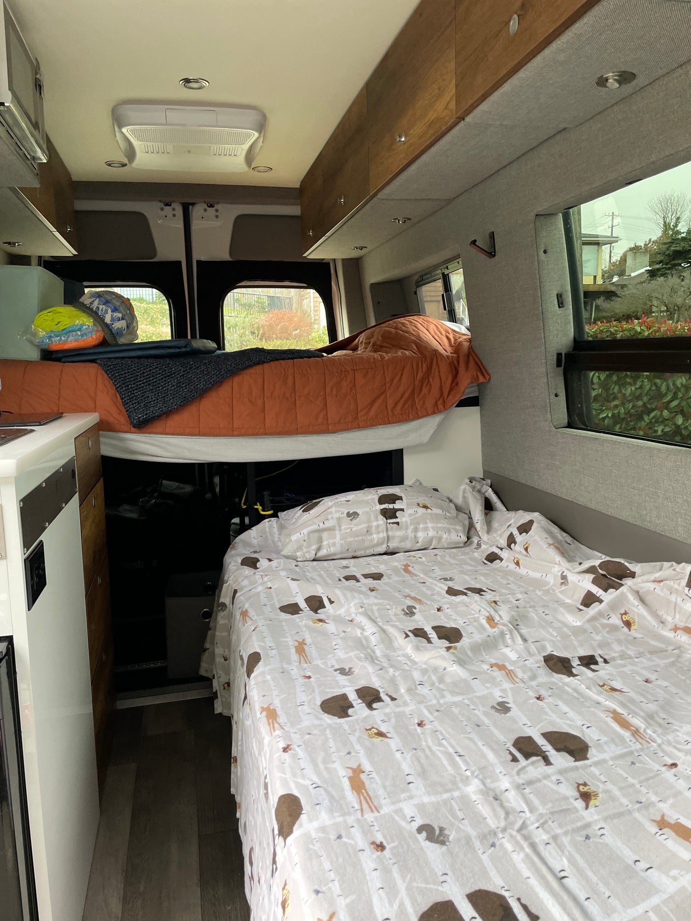 Inside a comfy rv rental, featuring elevated and lower bunk beds, kitchen area, and overhead storage.