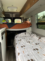 Inside a comfy rv rental, featuring elevated and lower bunk beds, kitchen area, and overhead storage.