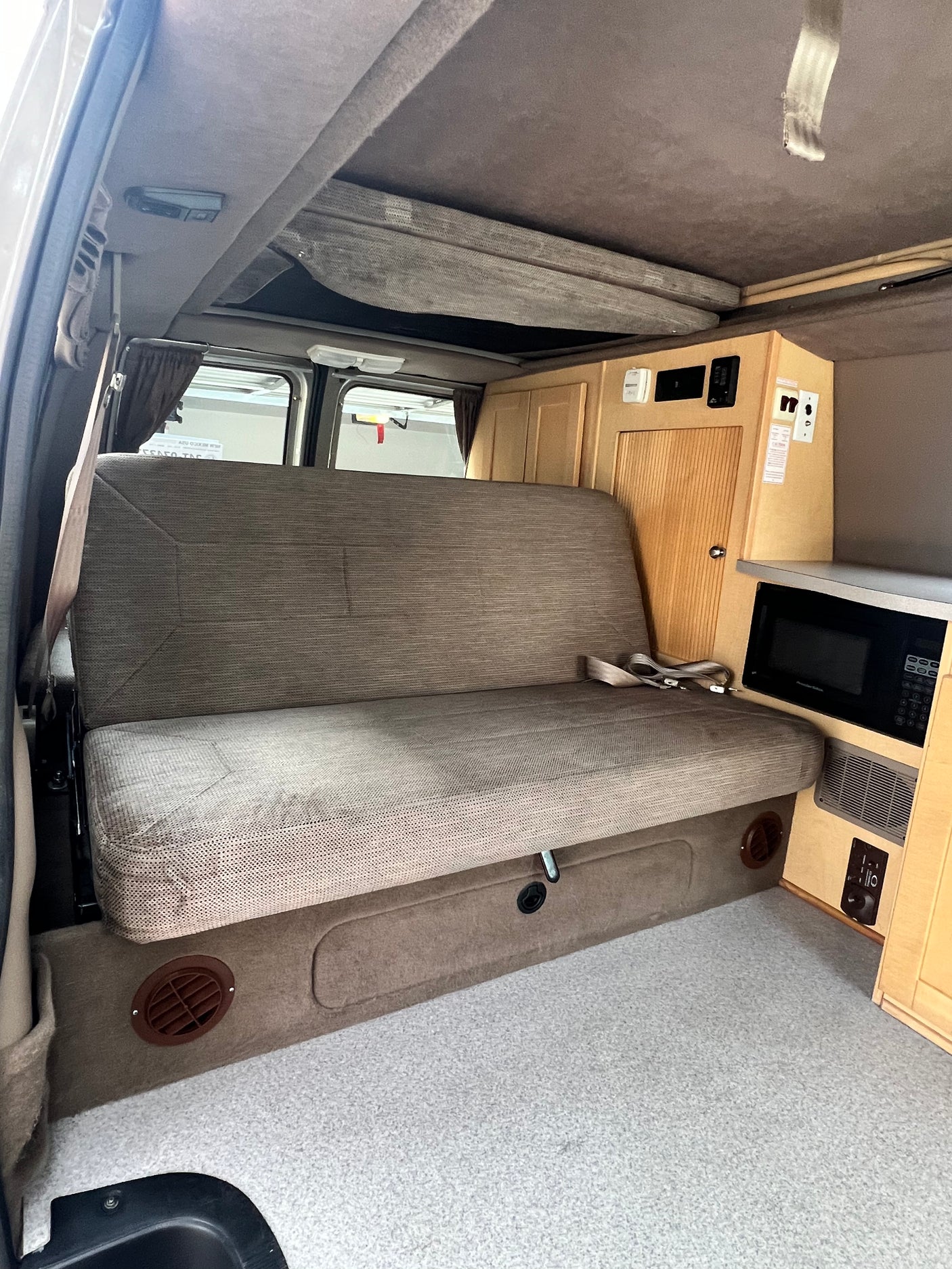 Interior of a practical rv rental with a large bench seat, overhead bunk, and built-in kitchenette including a microwave.