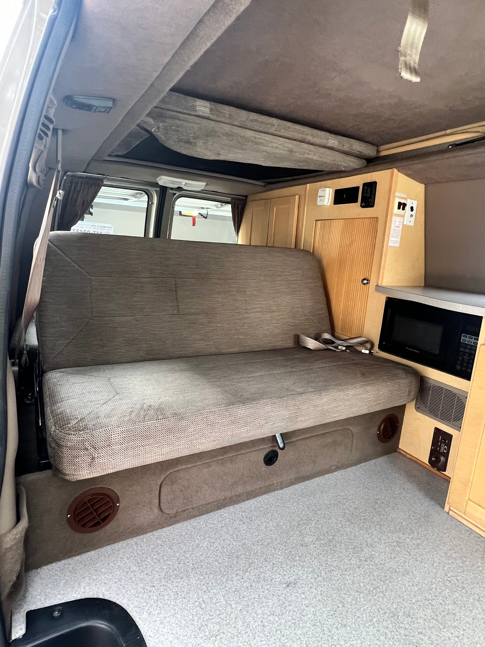 Interior of a practical rv rental with a large bench seat, overhead bunk, and built-in kitchenette including a microwave.