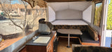 Pop-up camper RV rental interior featuring a large bed, dinette with table, and compact kitchen area with sink and stove.