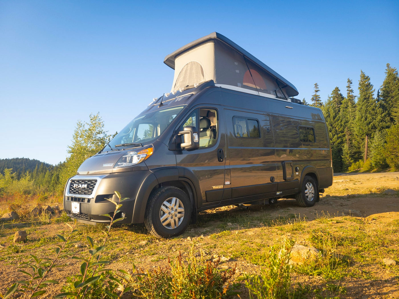  ready for adventure.|A dark camper van with a pop-top roof is parked on a dirt path at a sunny forest campsite — photo 11