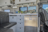 This compact RV rental interior features a kitchen with a sink, fridge, storage, and cozy seating, ideal for van life adventures.