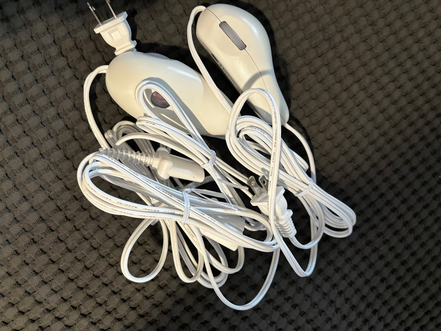 Essential for comfort in an rv rental: tangled white electric blanket controls and cords with a US plug on dark fabric.