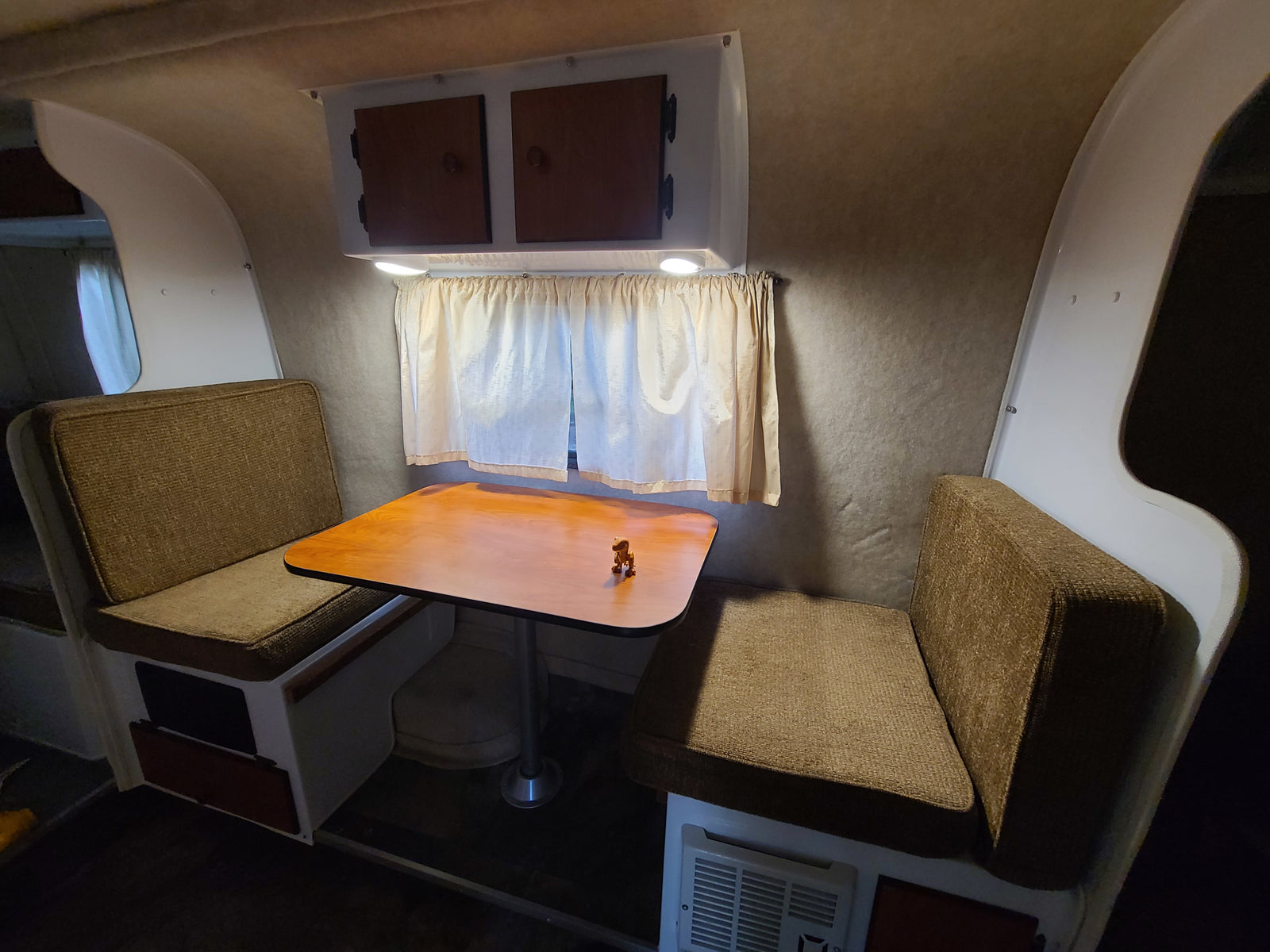 This RV rental features a cozy interior with a dinette, including two brown upholstered benches, a wooden table, and overhead cabinets.
