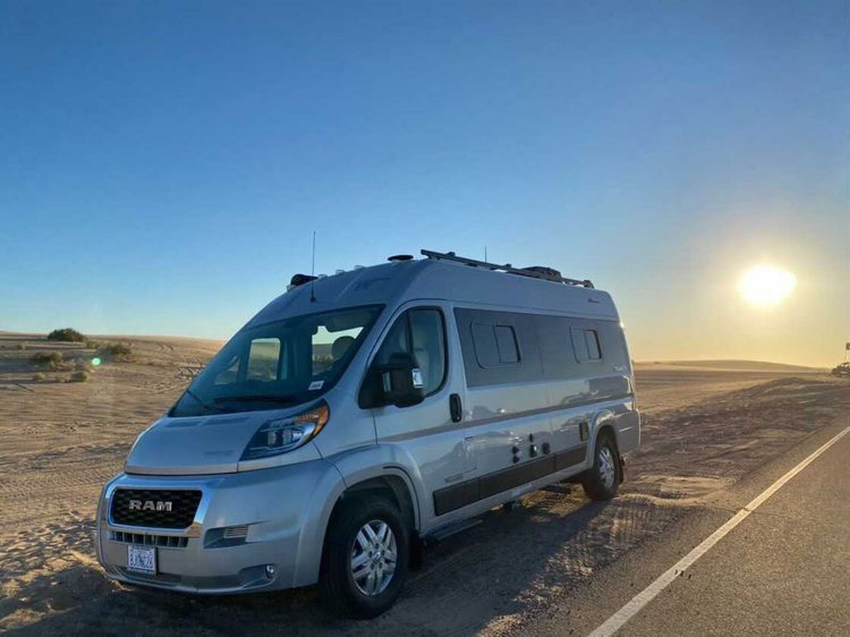Silver RV rental camper van at desert sunset. Parked by the road