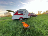 Teardrop RV rental & SUV camping in a grassy field with a campfire at sunset.