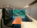 Explore this RV rental's versatile van interior. Features padded benches, dining table, storage, and a forest view.