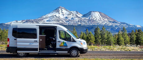 Experience scenic travels! This RV rental van is parked with its door open, showcasing snow-capped mountains and pine forests.