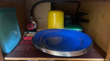 Essential RV rental kitchen cabinet with a propane regulator, blue plates, water bottle, and cookware.