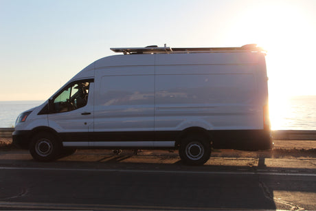 White RV rental van with rooftop solar, parked ocean-side at sunset. Ideal for coastal travel adventures.