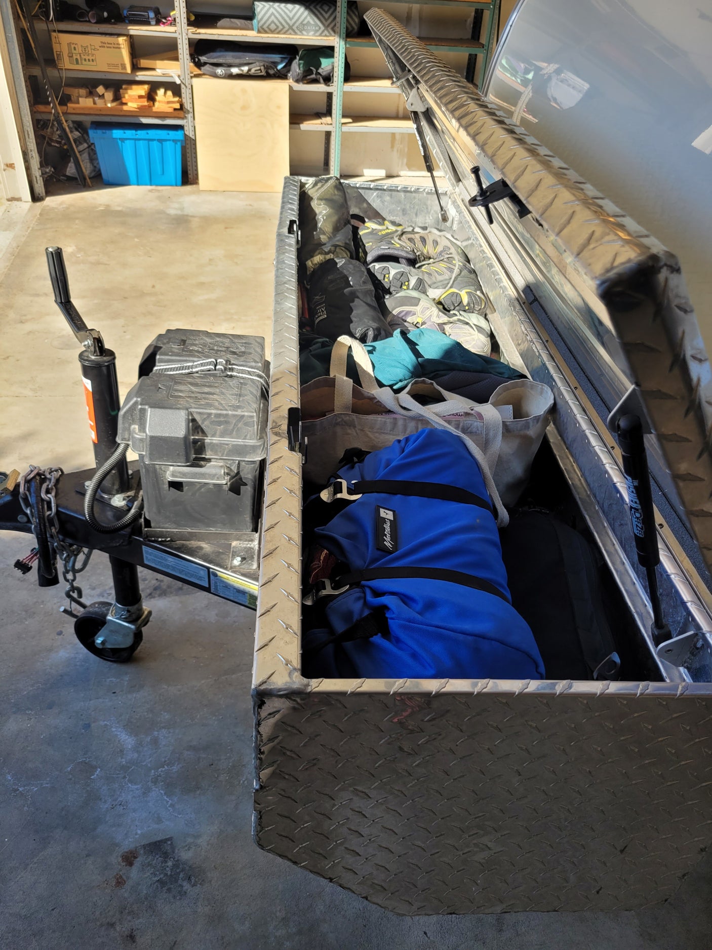 Trailer with open storage box for RV rental gear, packed with shoes, bags, and outdoor essentials in a garage.