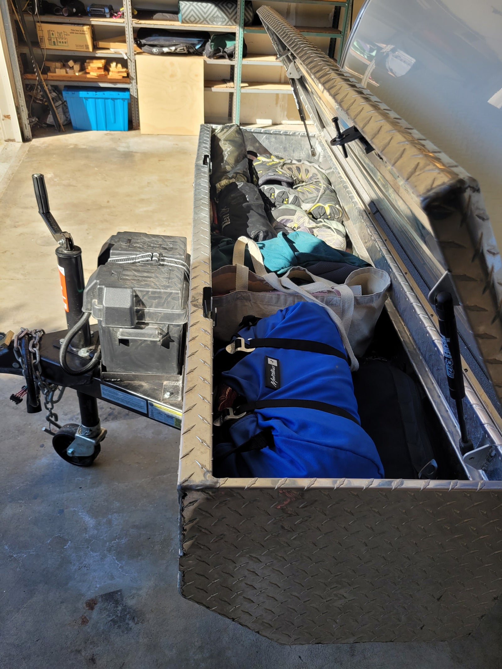 Trailer with open storage box for RV rental gear, packed with shoes, bags, and outdoor essentials in a garage.