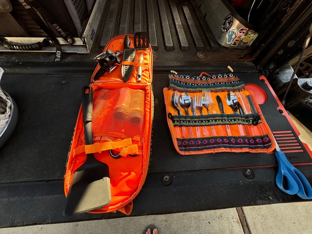 RV rental cooking setup: orange cases with spatula, knives, portable burner, and organized silverware for camping.
