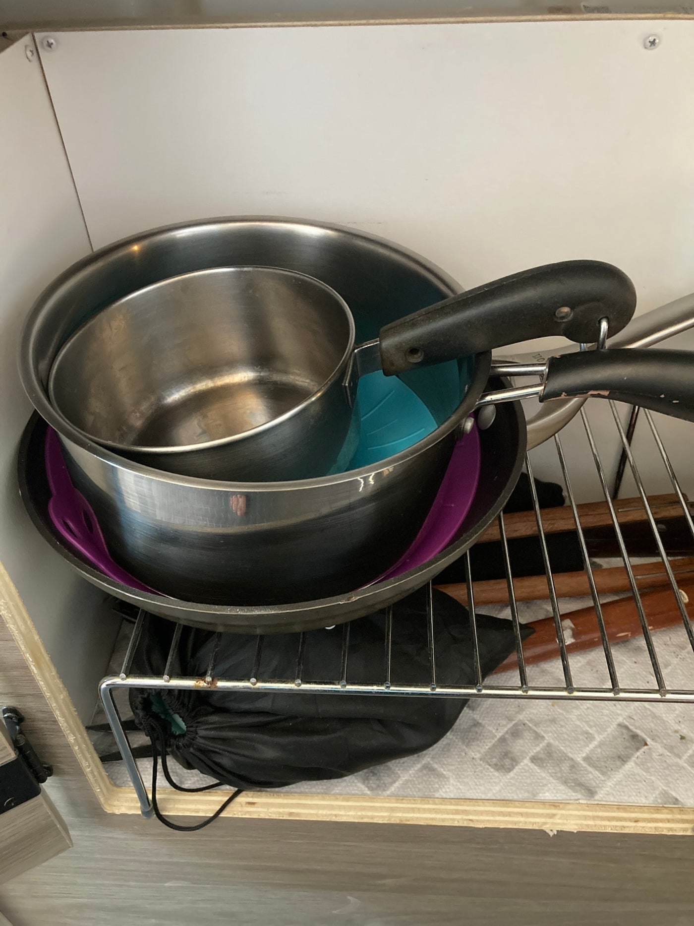 RV rental kitchenware: Stacked pots, pans, and utensils efficiently stored in a compact cabinet. — photo 18