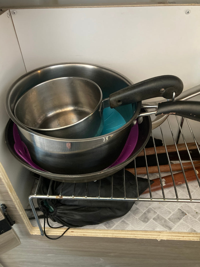 RV rental kitchenware: Stacked pots, pans, and utensils efficiently stored in a compact cabinet. — photo 18
