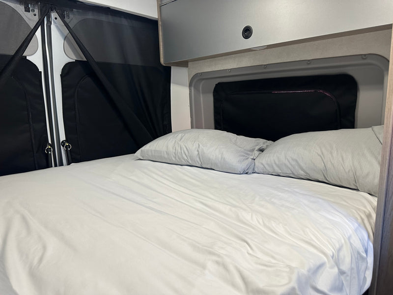 Comfortable **rv rental** bed with white sheets & grey pillows, featuring window screens and overhead cabinets. — photo 10