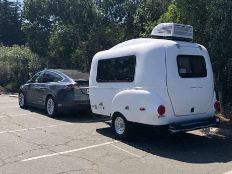 Gray Tesla towing a white Happier Camper trailer with rooftop AC and Road Shower 4, an excellent rv rental setup.