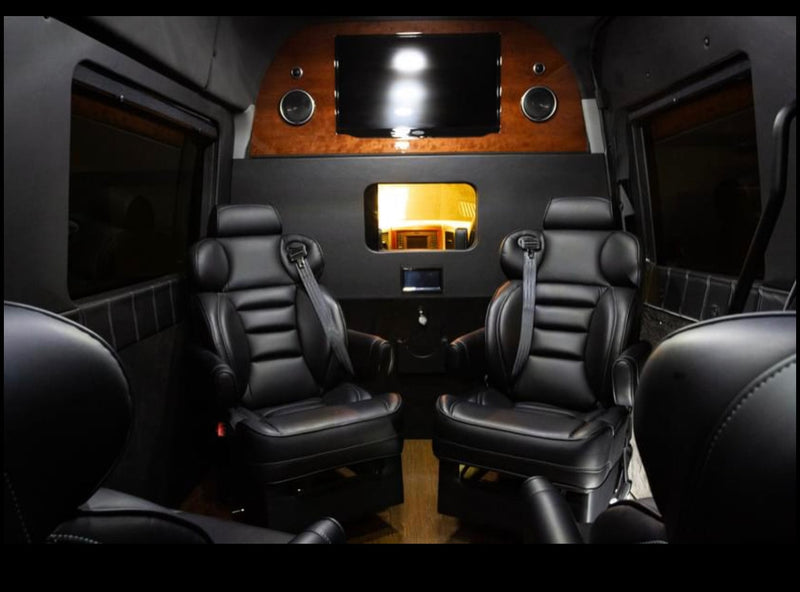 Premium RV rental interior featuring two plush black leather captain's chairs, a large TV, and custom wood details. — photo 5
