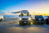 Enjoy beach sunsets with an RV rental! This Mercedes camper van is parked by the ocean at dusk, perfect for vacation.