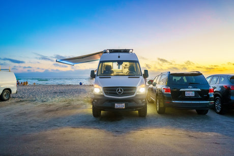 Enjoy beach sunsets with an RV rental! This Mercedes camper van is parked by the ocean at dusk, perfect for vacation.